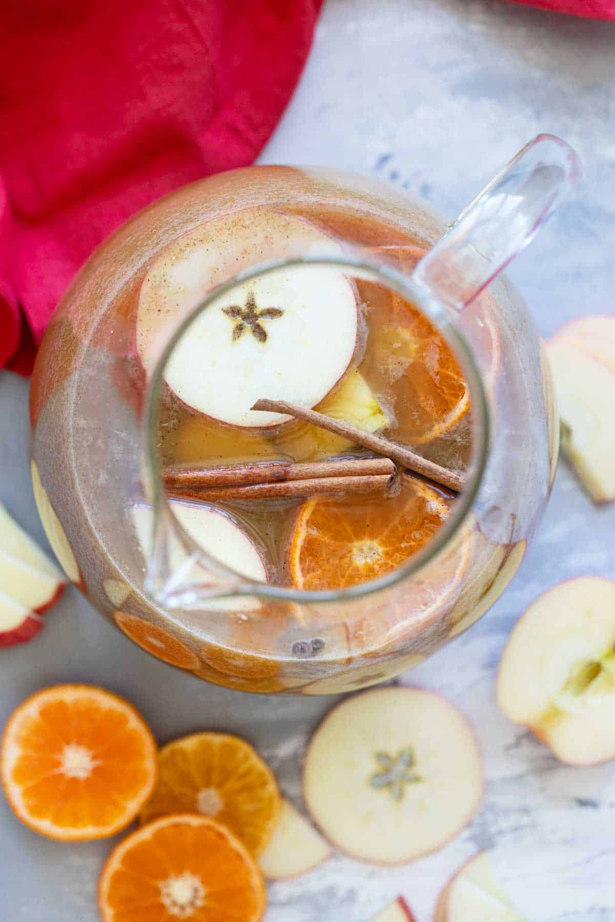 Pitcher filled with Apple Cider Punch, with apple slices and orange slices.