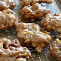 Glazed Apple Fritters on a cooling rack over parchment paper.