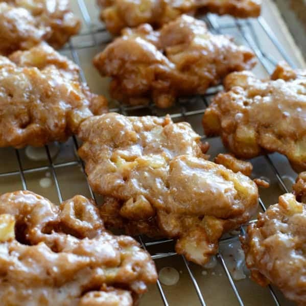 Glazed Apple Fritters on a cooling rack over parchment paper.