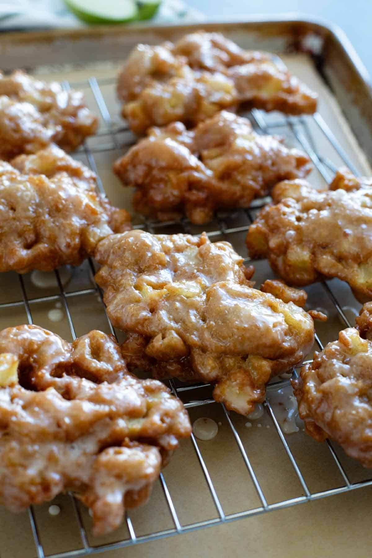 Glazed Apple Fritters on a cooling rack over parchment paper.