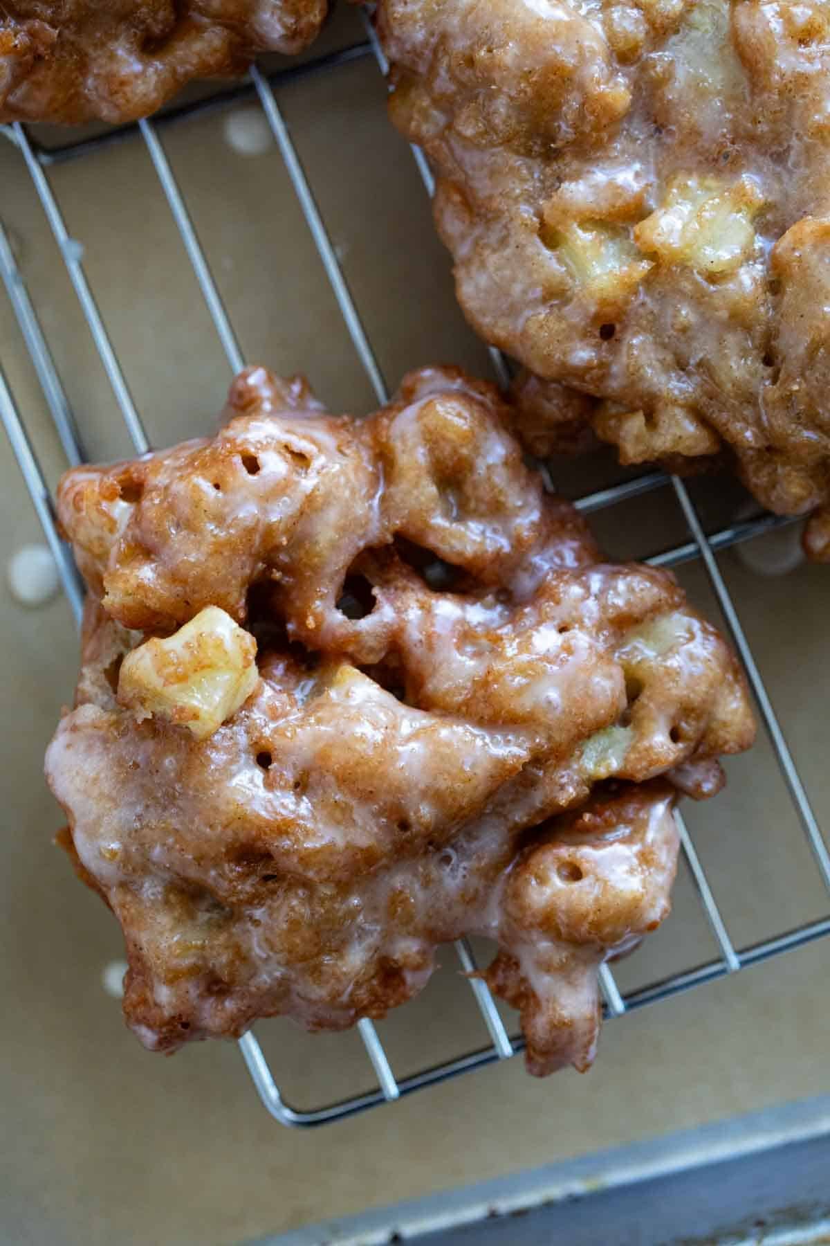 Glazed apple fritters on a cooling rack.