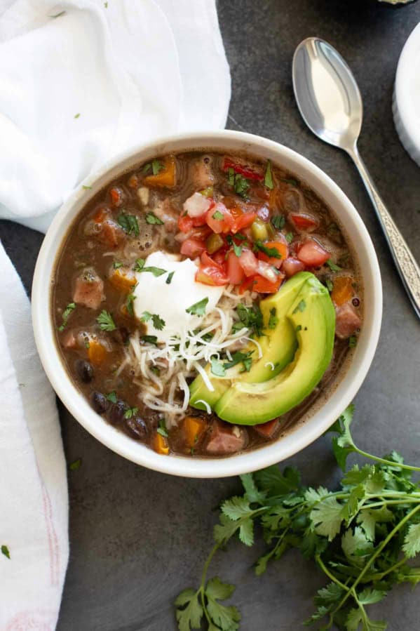 Bowl of Black Bean and Ham Soup topped with sour cream, pico de Gallo, cheese, and avocado.