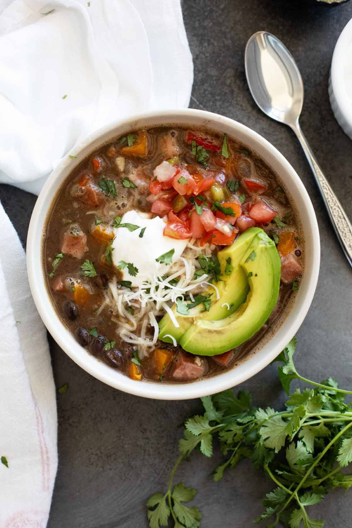 Bowl of Black Bean and Ham Soup topped with sour cream, pico de Gallo, cheese, and avocado.