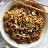 Bowl filled with Mongolian Ground Beef Noodles with chopsticks on the side.
