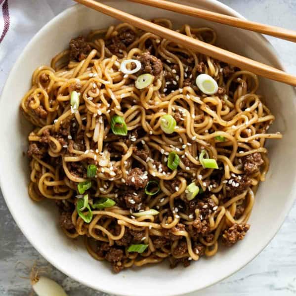 Bowl filled with Mongolian Ground Beef Noodles with chopsticks on the side.