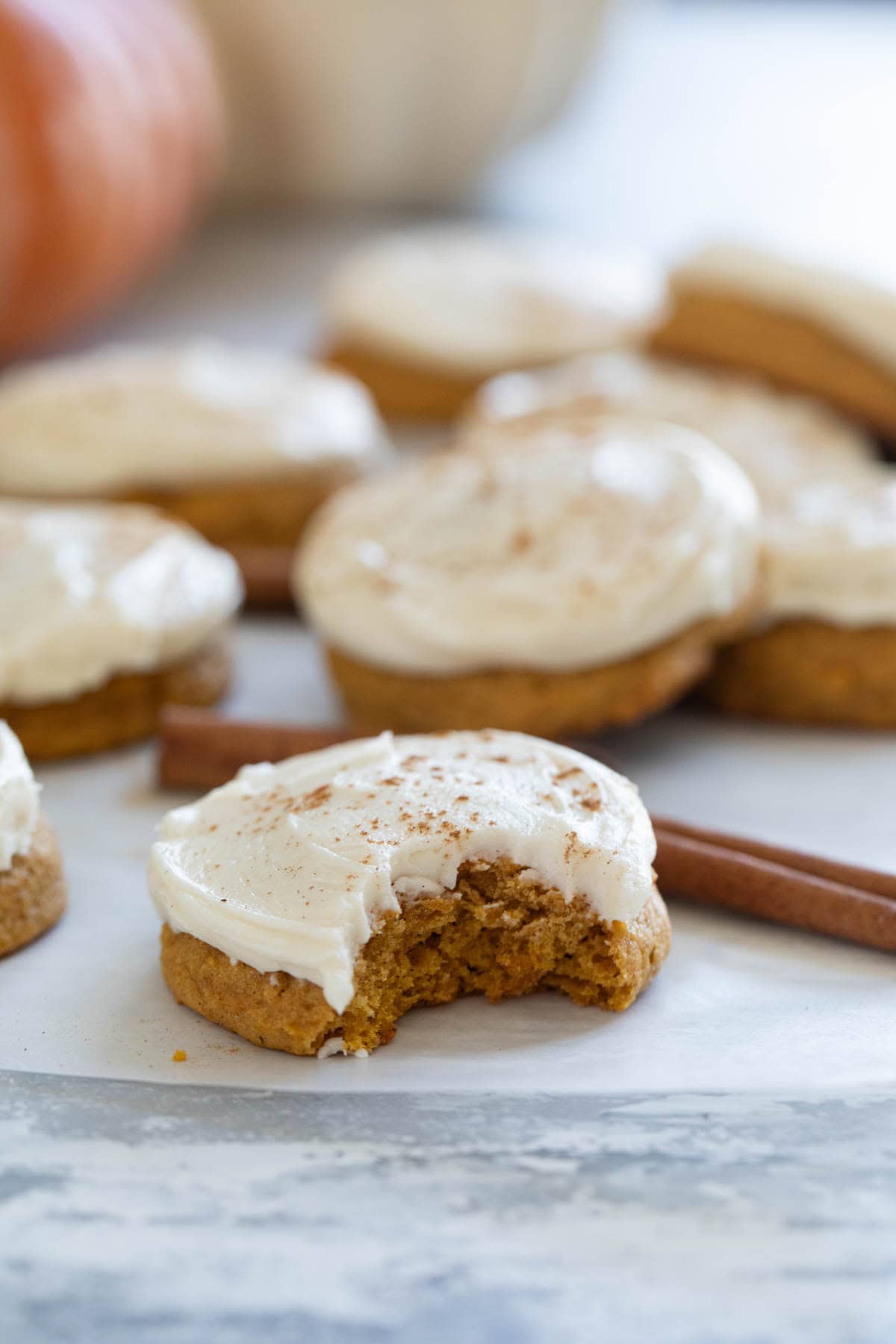 Pumpkin Cookies with Cream Cheese Frosting with a bite taken from one cookie.