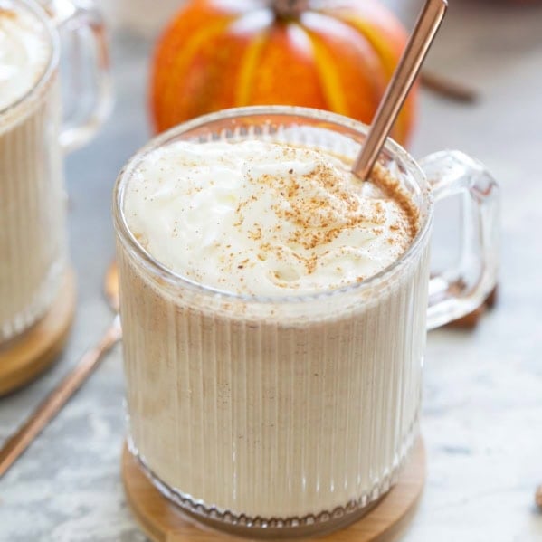 Pumpkin spice steamer in a glass mug, topped with fresh whipped cream and spices.