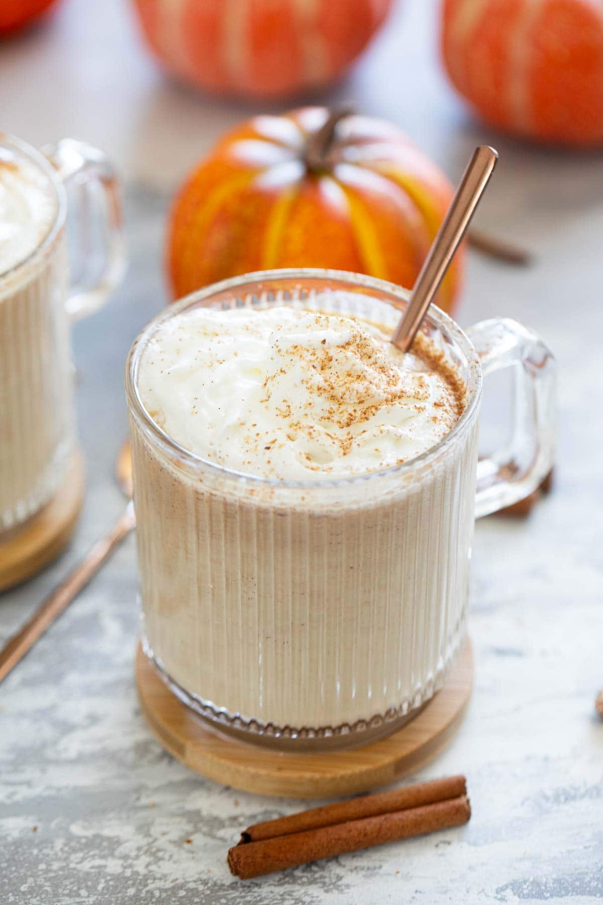 Pumpkin spice steamer in a glass mug, topped with fresh whipped cream and spices.