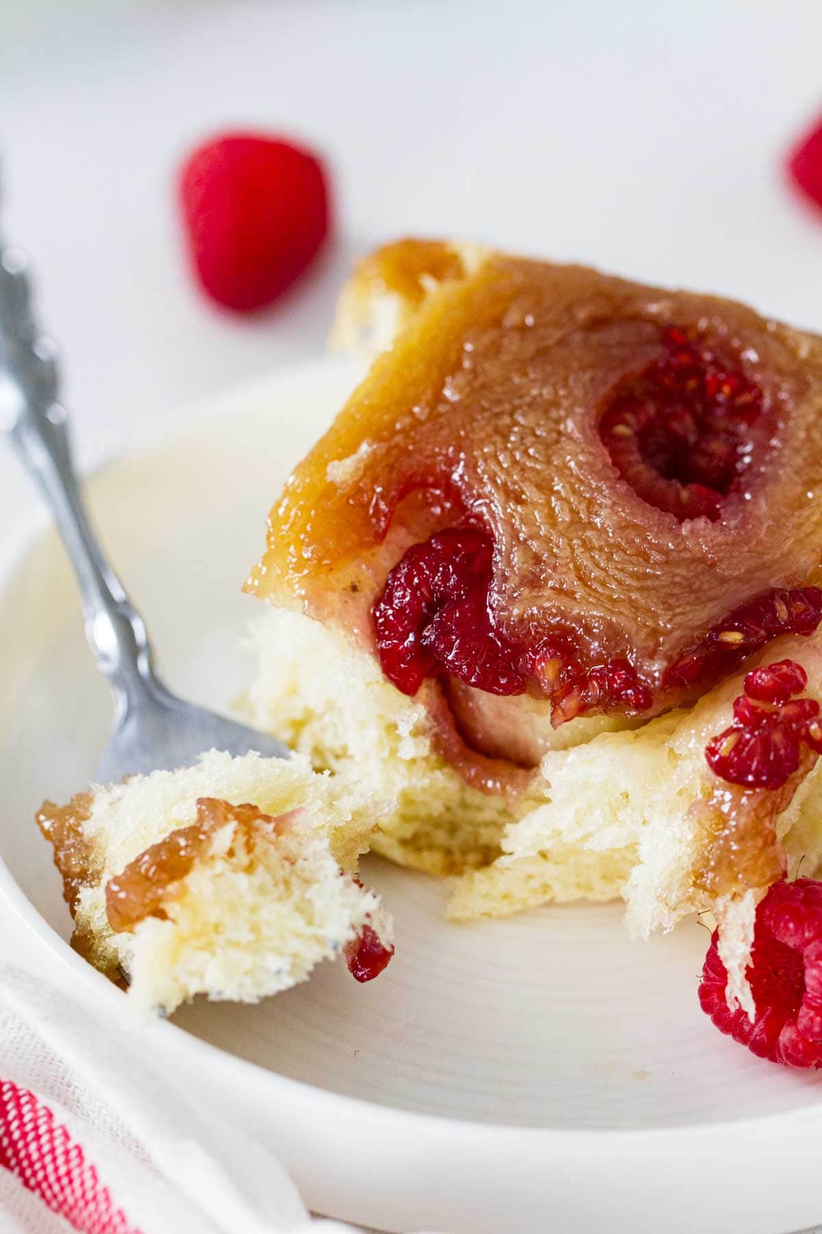 Raspberry Caramel Sticky Bun on a plate with a bite taken from it.