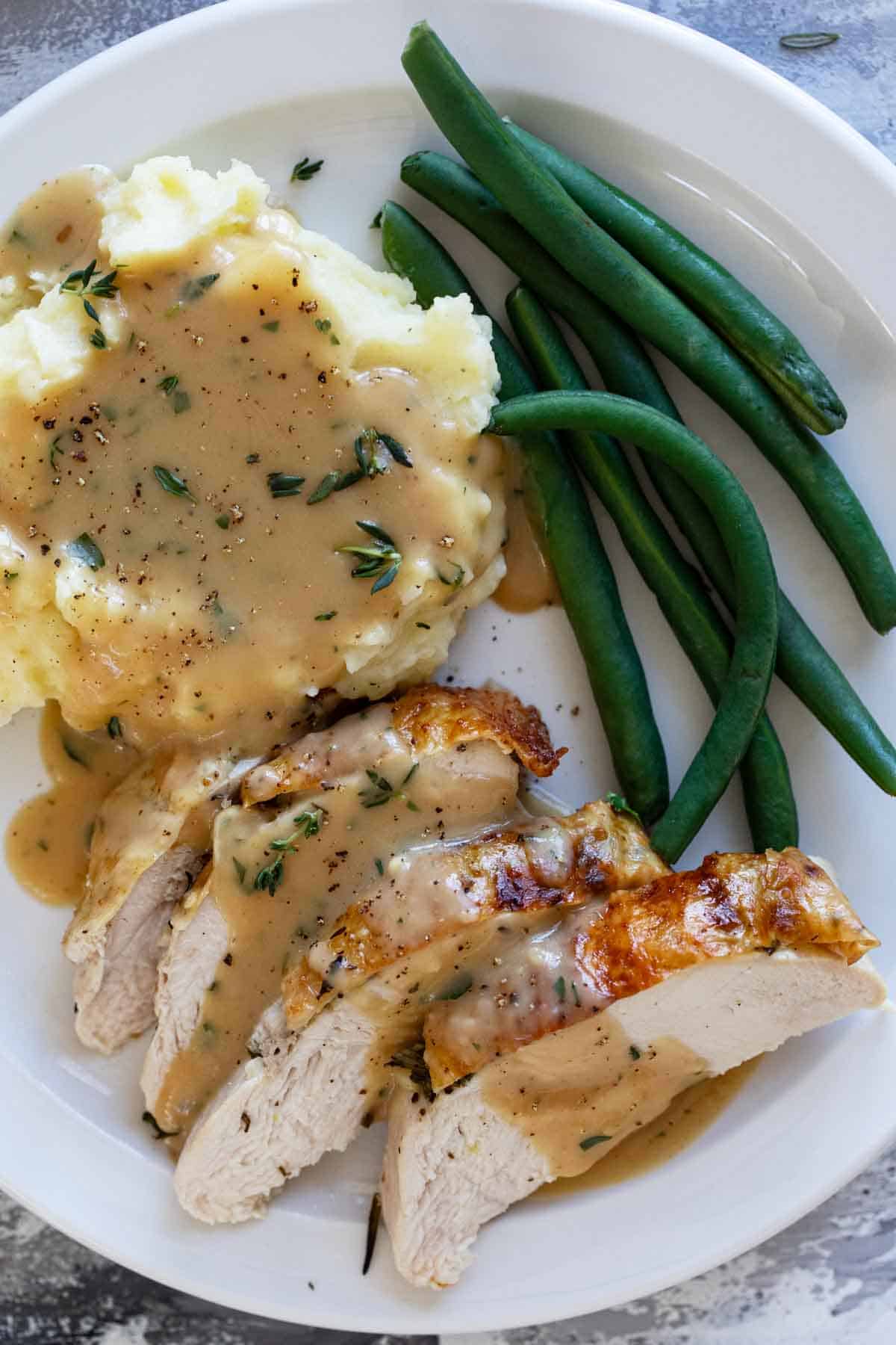 Sliced roast turkey with gravy, mashed potatoes, and green beans.