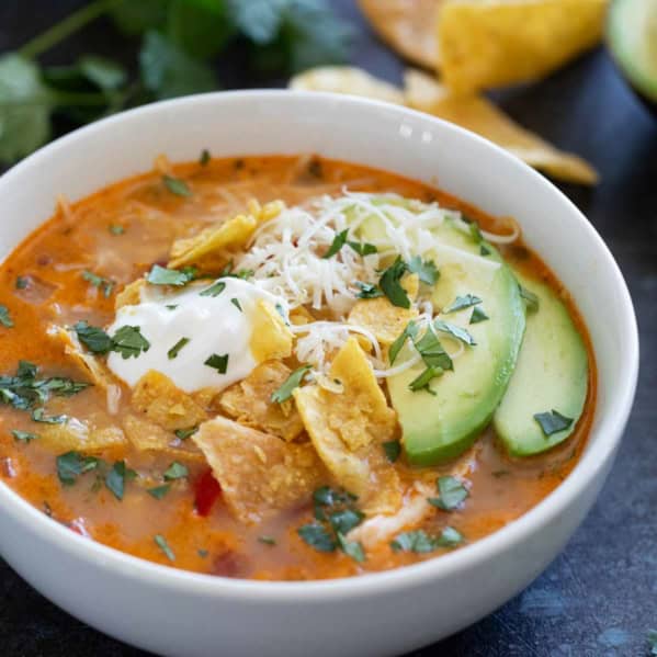 Bowl of slow cooker chicken enchilada soup topped with cheese, tortilla chips, sour cream, cilantro, and avocado.
