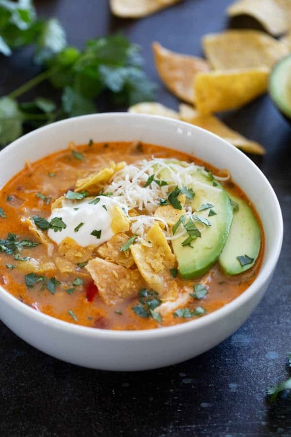 Bowl of slow cooker chicken enchilada soup topped with cheese, tortilla chips, sour cream, cilantro, and avocado.
