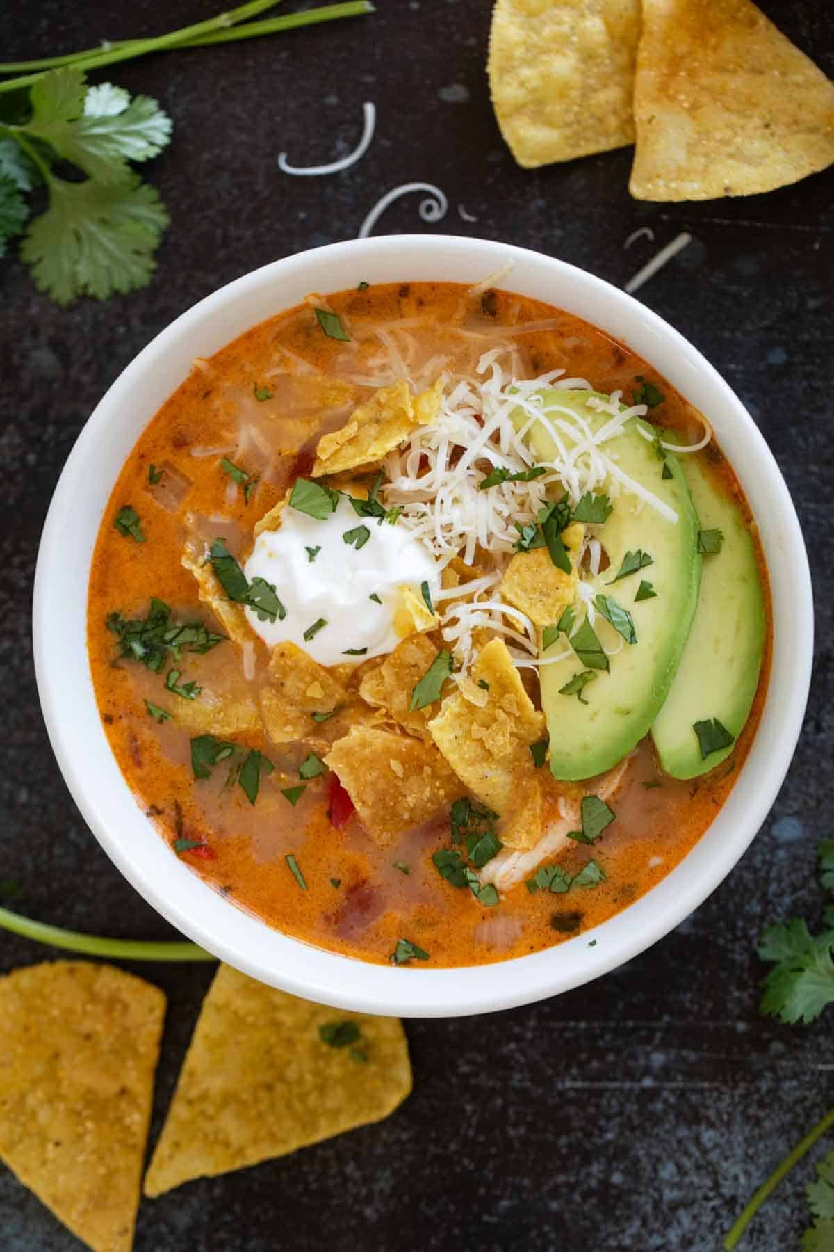 Bowl of slow cooker chicken enchilada soup topped with tortilla chips, sour cream, and avocado.