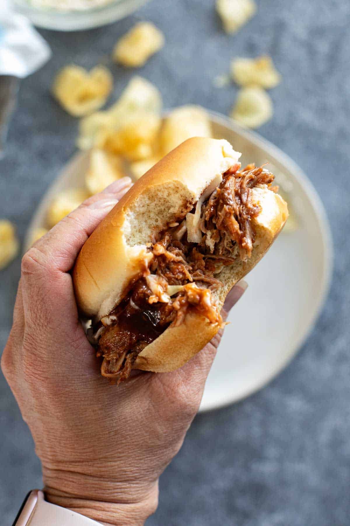 Holding a sandwich filled with pulled pork on a bun.