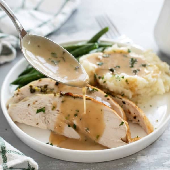 Spooning turkey gravy over slices of turkey.