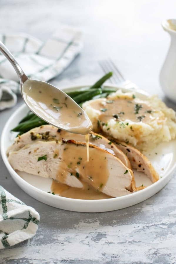 Spooning turkey gravy over slices of turkey.
