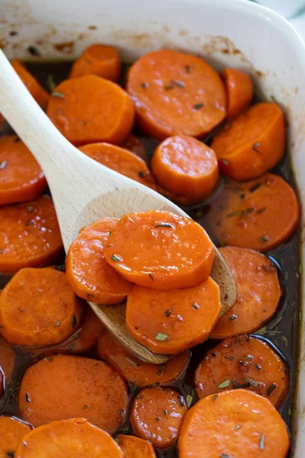 Scooping candied sweet potatoes with a wooden serving spoon.