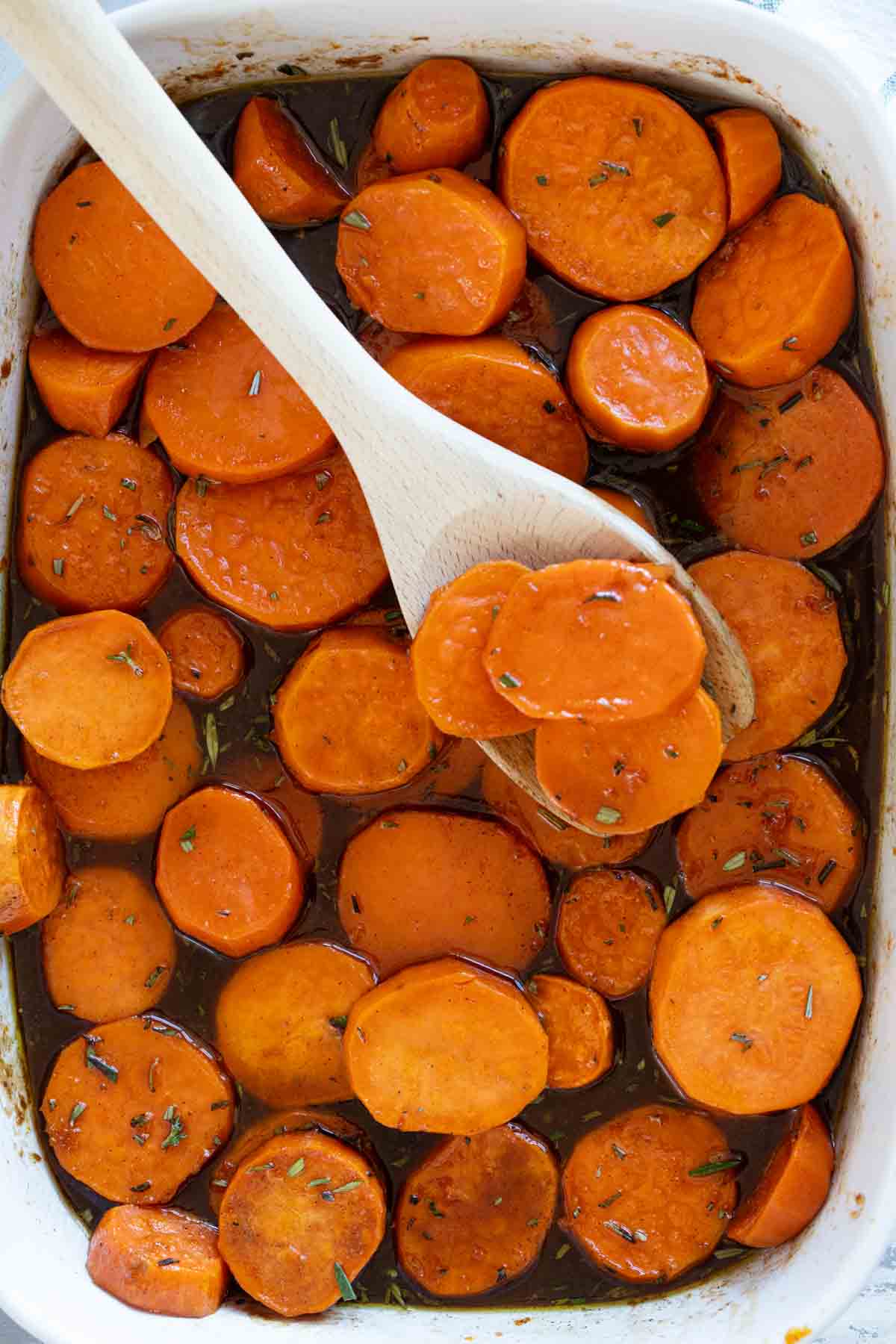 Baking dish full of candied sweet potatoes topped with fresh rosemary.