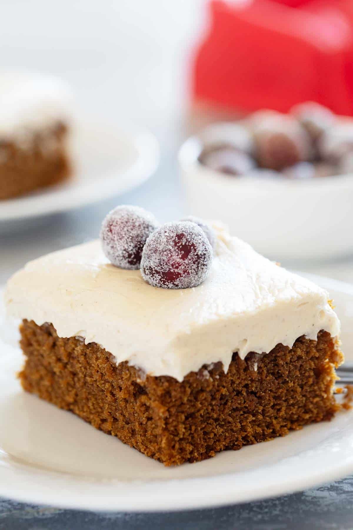 Slice of Gingerbread Cake with Brown Sugar Cream Cheese Frosting, topped with sugared cranberries.