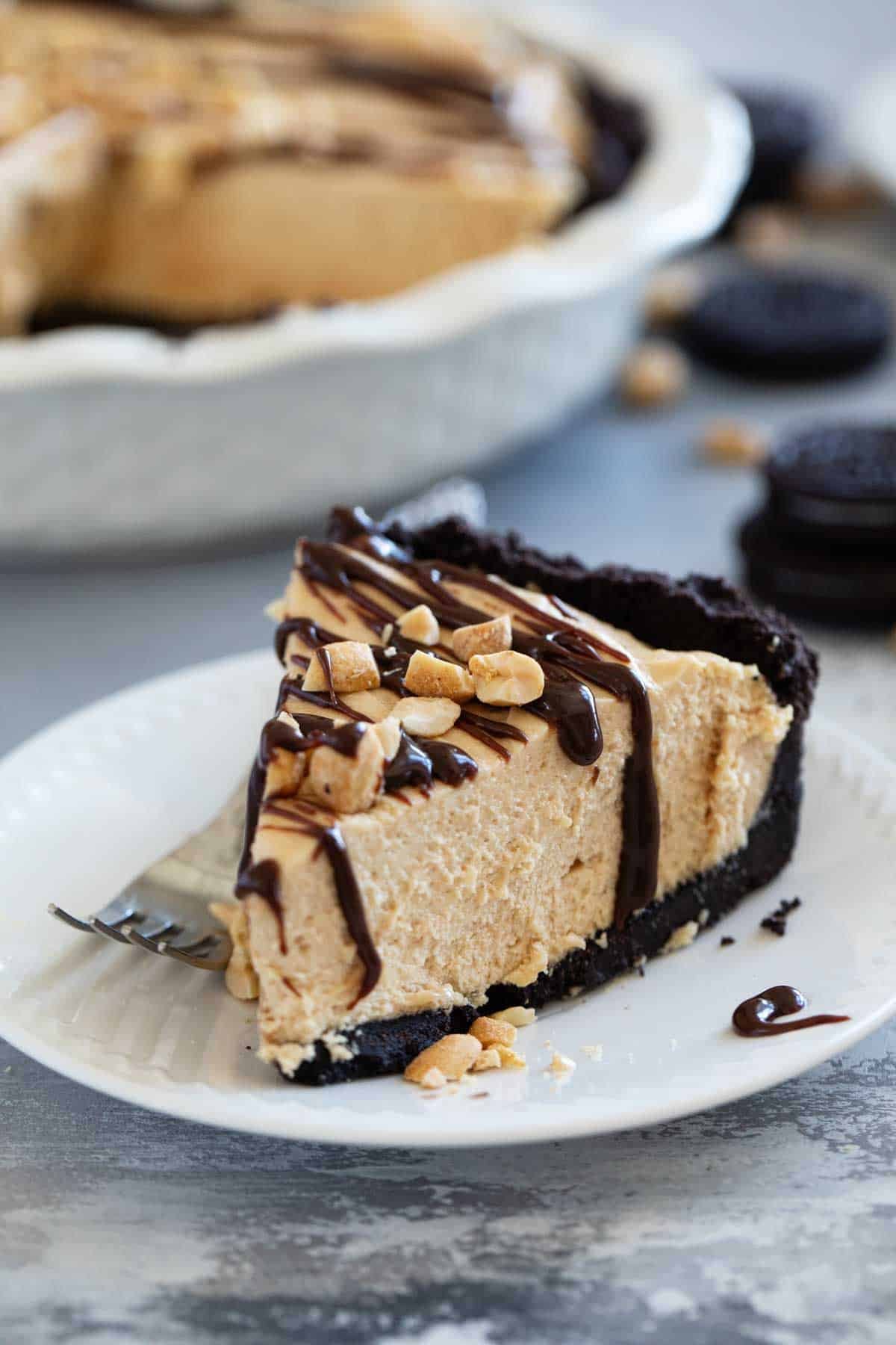 Slice of Peanut Butter Pie on a plate, topped with hot fudge sauce and peanuts.