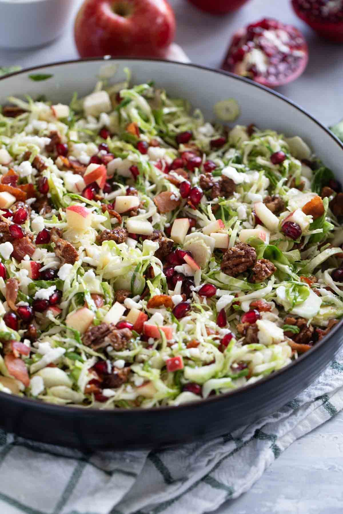 Bowl with shaved Brussels sprout salad with apples, pomegranates, candied nuts, and bacon.
