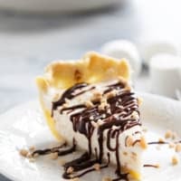 Slice of Toffee Marshmallow Pie with hot fudge drizzled over the top, and sprinkled with toffee pieces.
