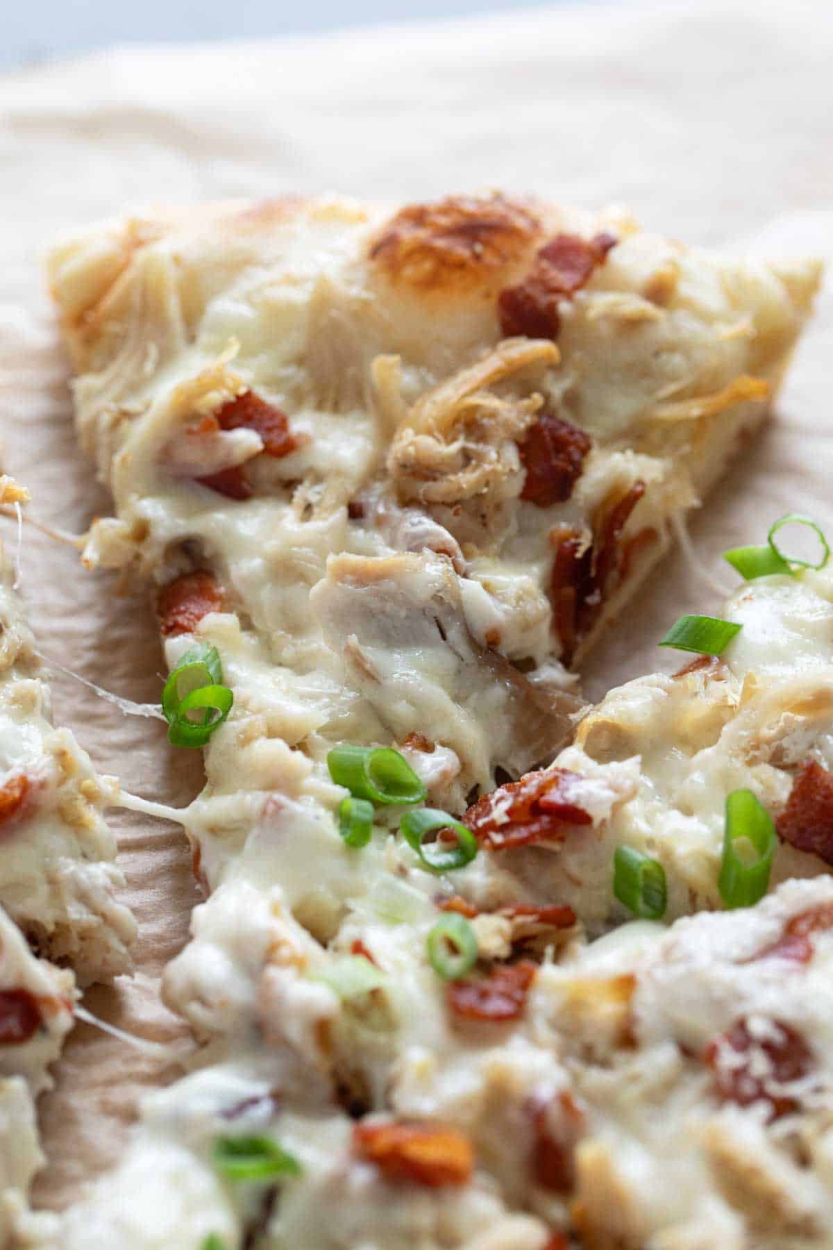 Slice of Chicken Alfredo Pizza topped with bacon.
