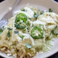 Plate with two Enchiladas Suizas topped with jalapeños, onions, and cilantro.