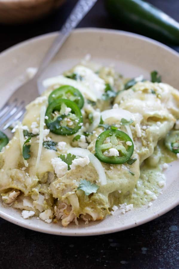 Plate with two Enchiladas Suizas topped with jalapeños, onions, and cilantro.