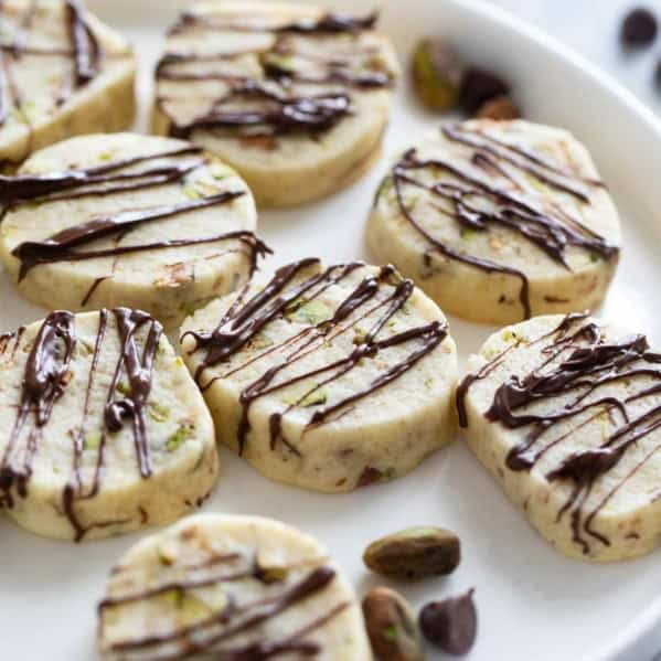 Pistachio Cookies drizzled with chocolate on a white plate.