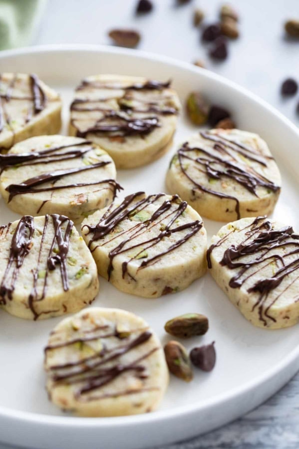 Pistachio Cookies drizzled with chocolate on a white plate.