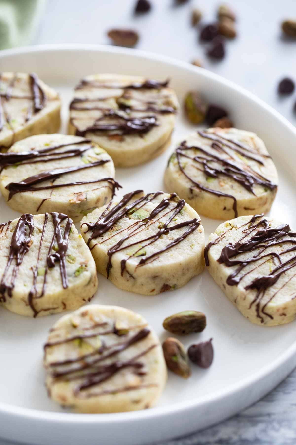 Pistachio Cookies drizzled with chocolate on a white plate.