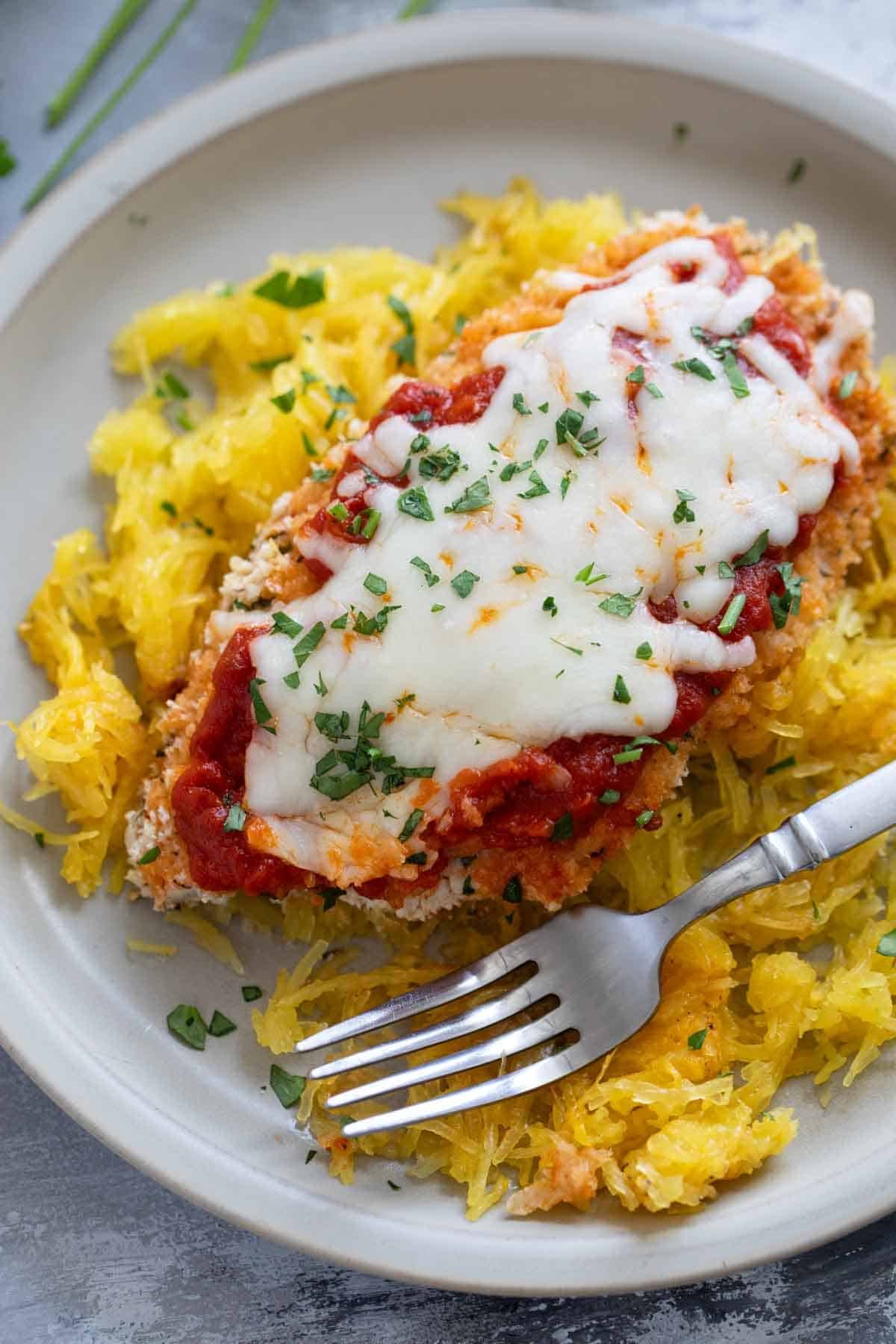 Baked Chicken Parmesan over spaghetti squash with a fork.
