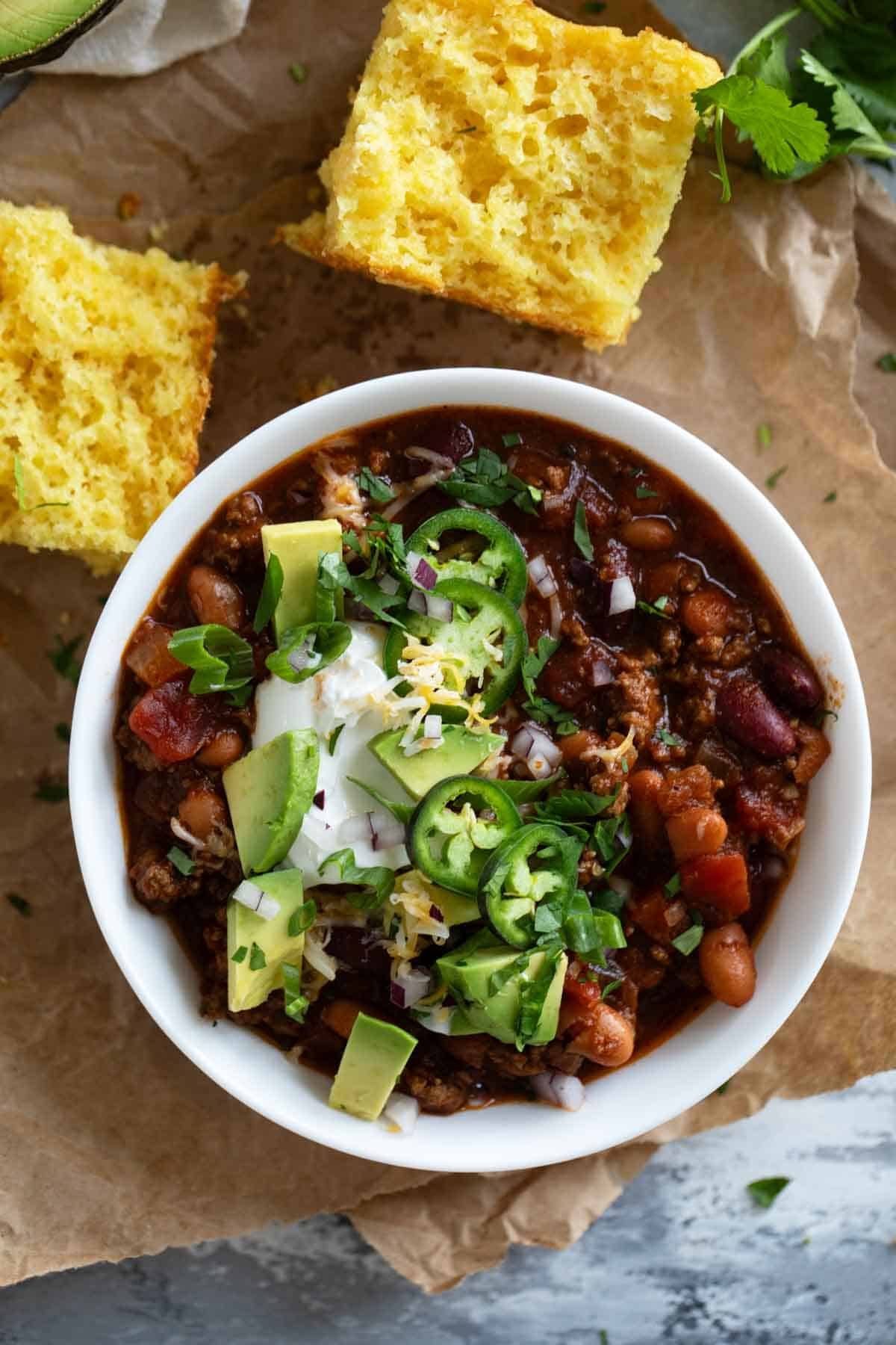 Bowl of crock pot chili topped with jalapeños, sour cream, avocado, and cheese.
