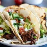 Ground Beef Tacos topped with lettuce, tomatoes, cheese, onions, and avocado.