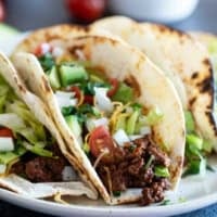 Ground Beef Tacos topped with lettuce, tomatoes, cheese, onions, and avocado.