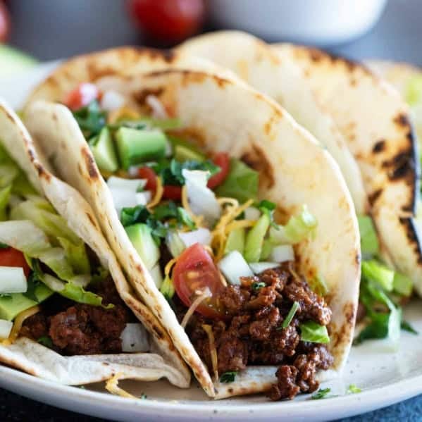Ground Beef Tacos topped with lettuce, tomatoes, cheese, onions, and avocado.