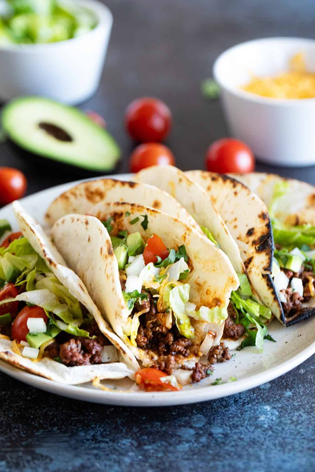 Ground beef tacos on a plate with a bite taken from one taco.