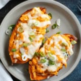 Two twice baked buffalo chicken sweet potatoes topped with green onions on a plate.