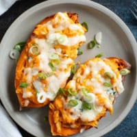 Two twice baked buffalo chicken sweet potatoes topped with green onions on a plate.