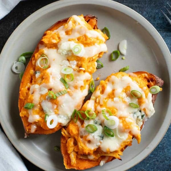 Two twice baked buffalo chicken sweet potatoes topped with green onions on a plate.