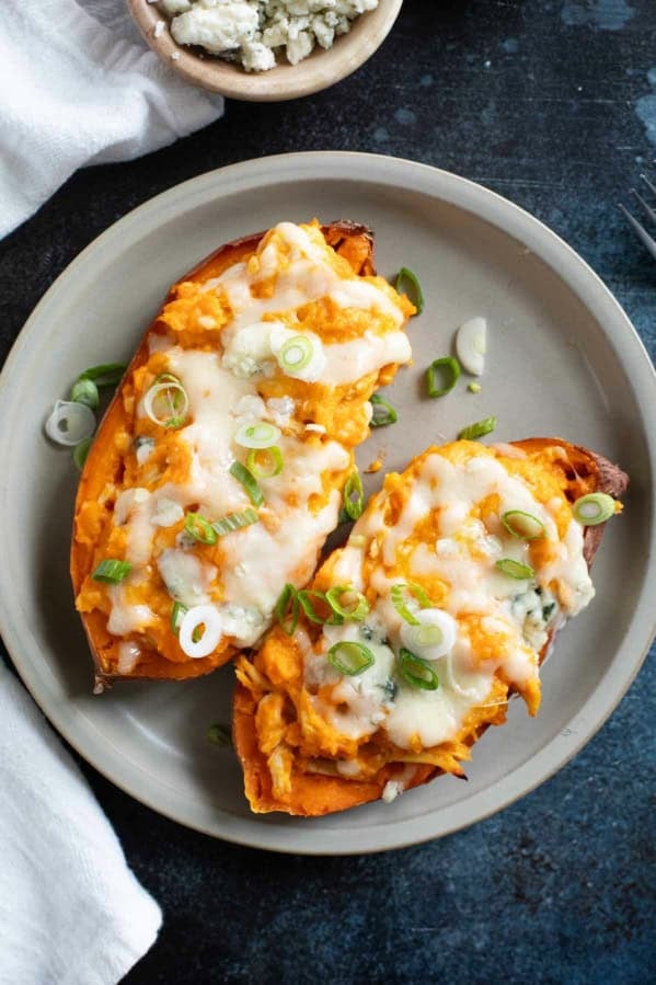 Two twice baked buffalo chicken sweet potatoes topped with green onions on a plate.