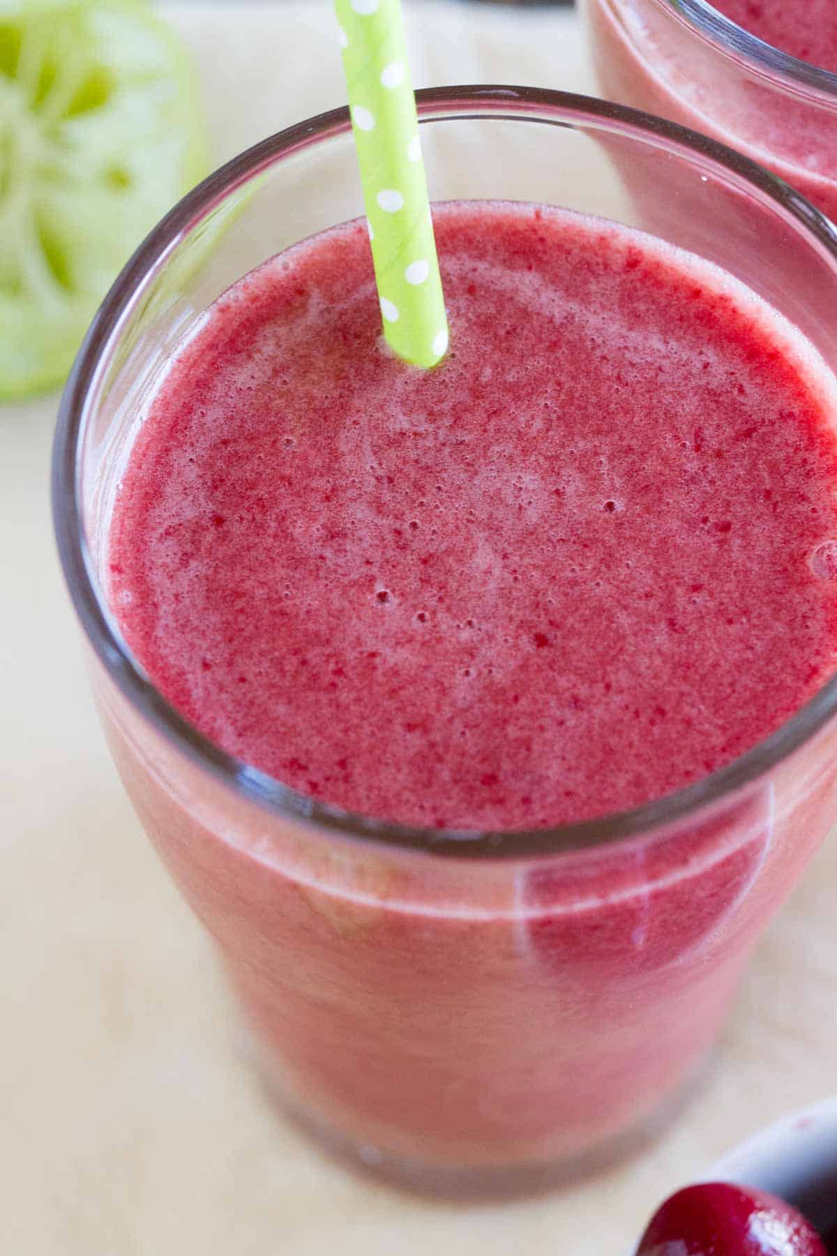 Cherry Coconut Smoothie in a glass with a green straw.