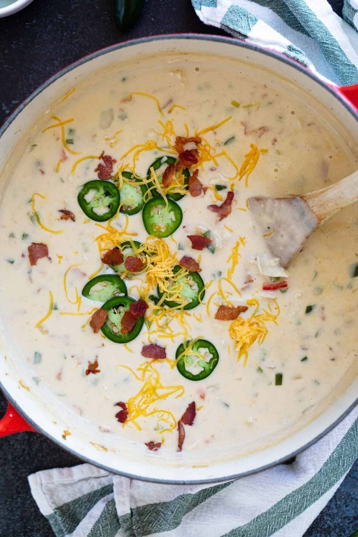 Dutch oven filled with Jalapeno Popper Soup topped with cheese, bacon, and jalapeños.