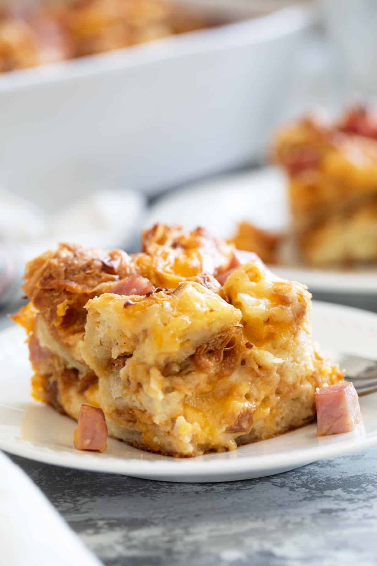 Slice of Croissant Breakfast Casserole with ham and cheese on a plate.