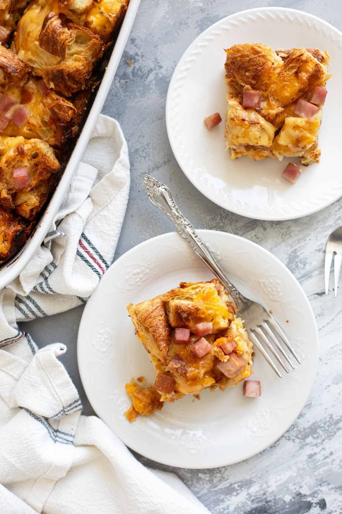 Two slices of Croissant Breakfast Casserole on plates with forks.