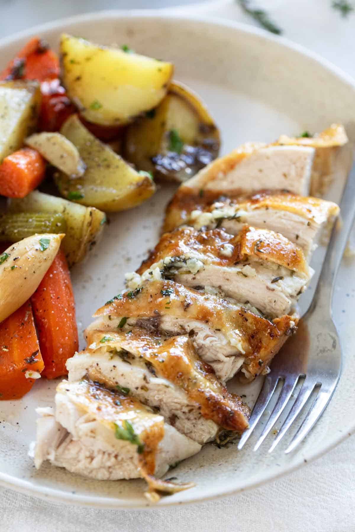 Sliced garlic roast chicken on a plate with vegetables.