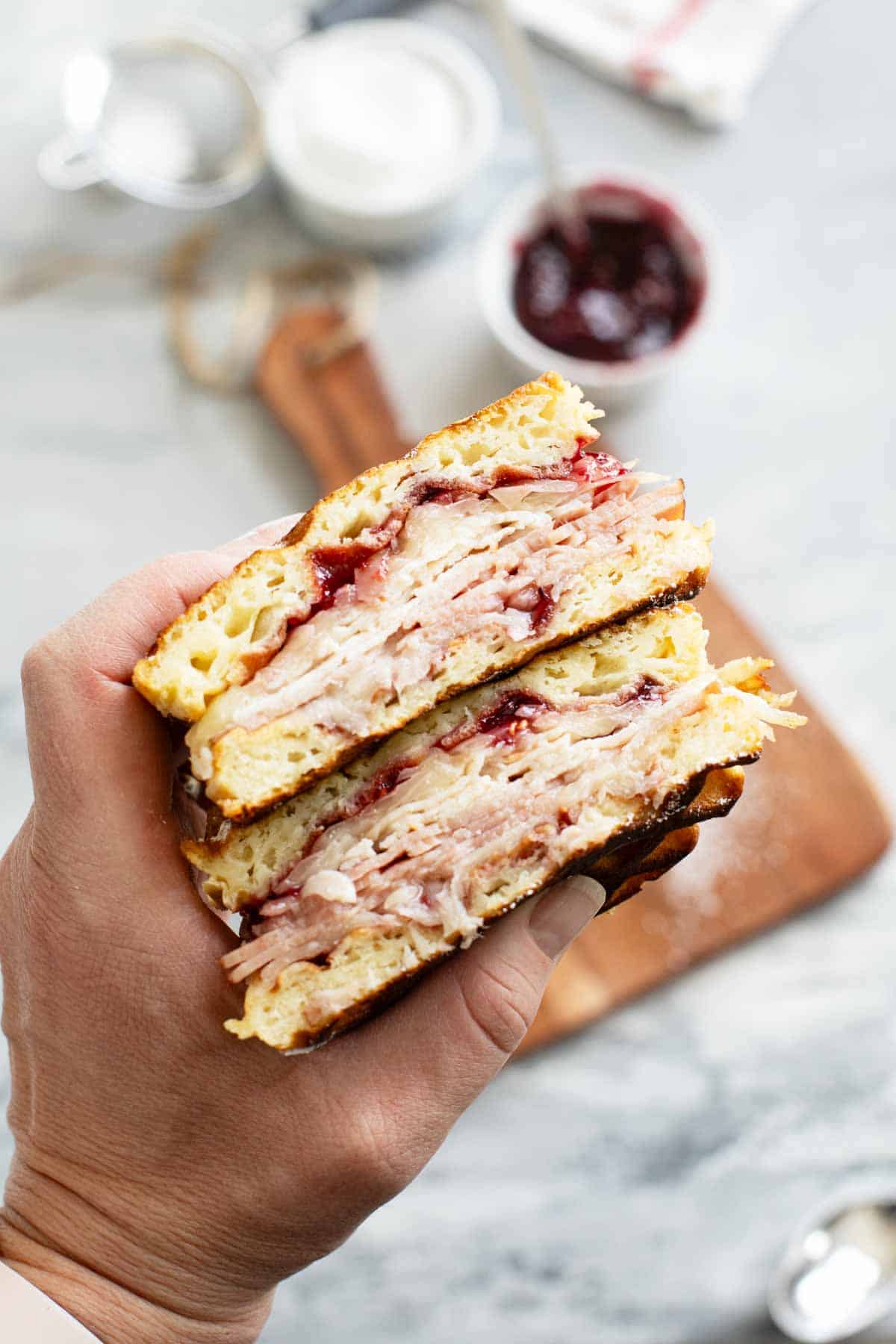Hand holding a Monte Cristo waffle sandwich that is cut in half.