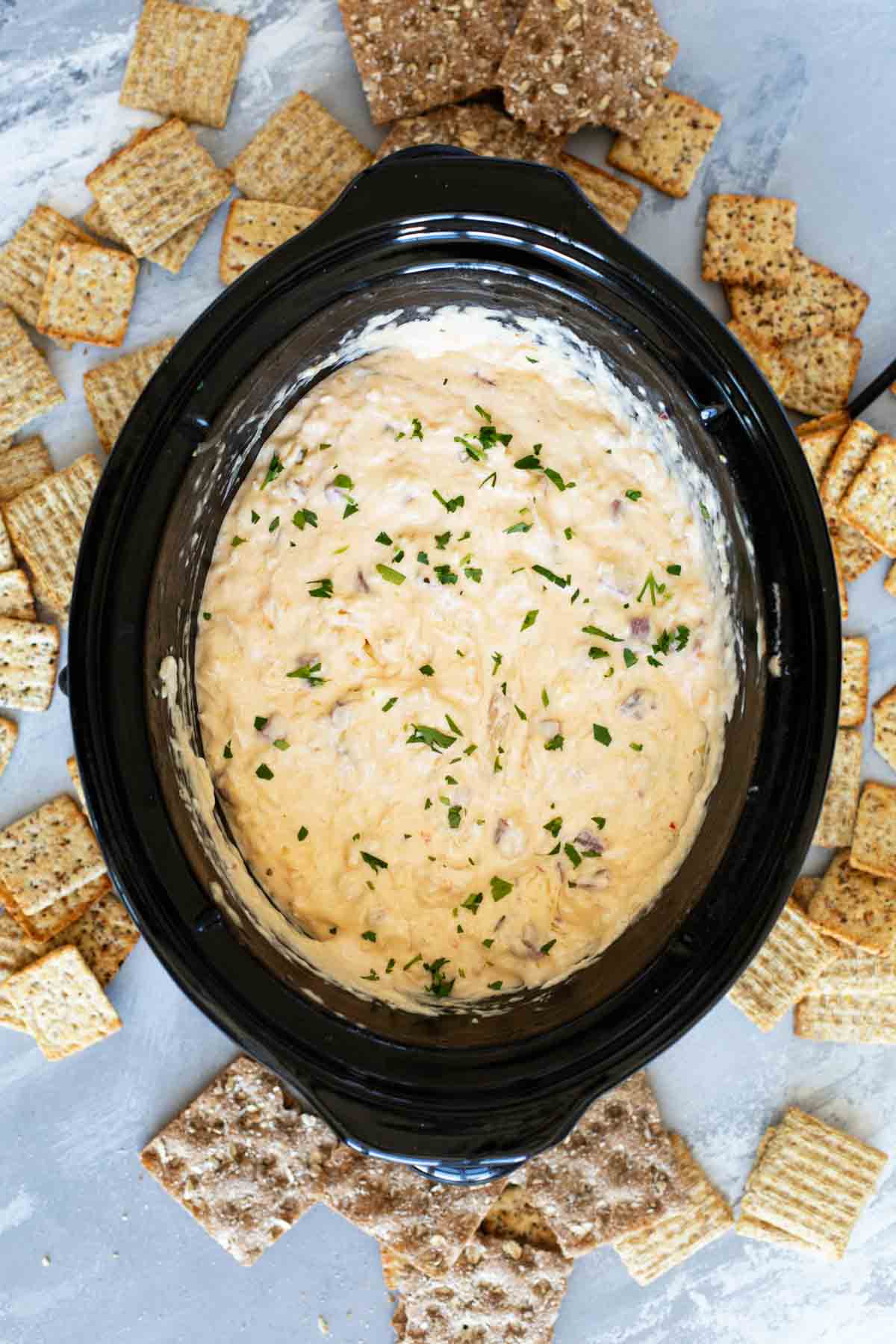 Slow cooker filled with reuben dip surrounded by assorted crackers.