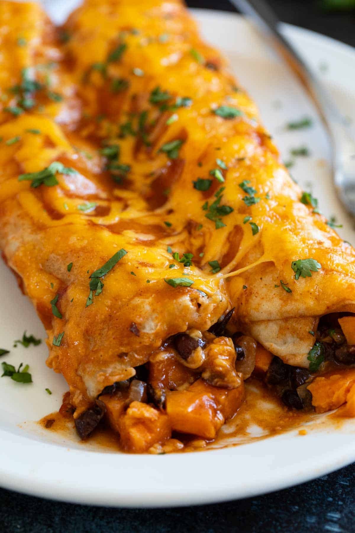 Two sweet potato and black bean enchiladas on a plate with a bite taken from one.